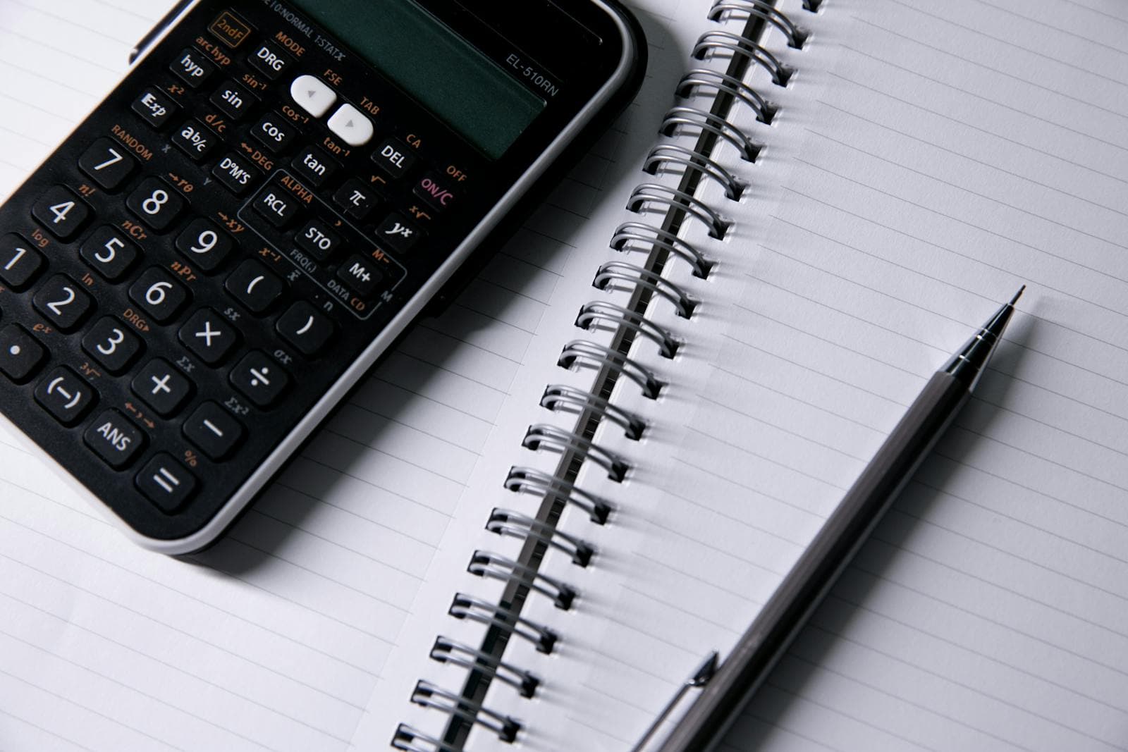 Open ruled notebook, desk calculator, and pen arranged on a workspace.
