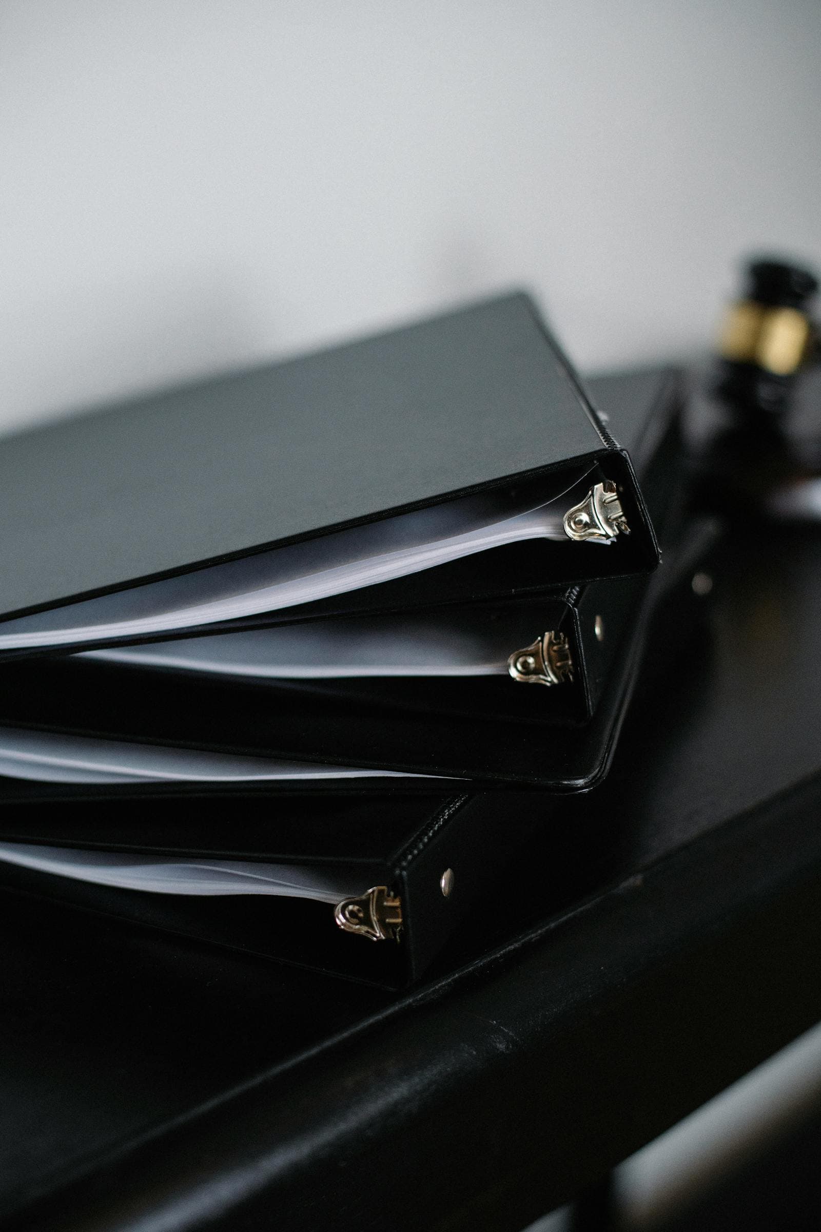 Neatly stacked black office binders filled with documents on a wooden desk.