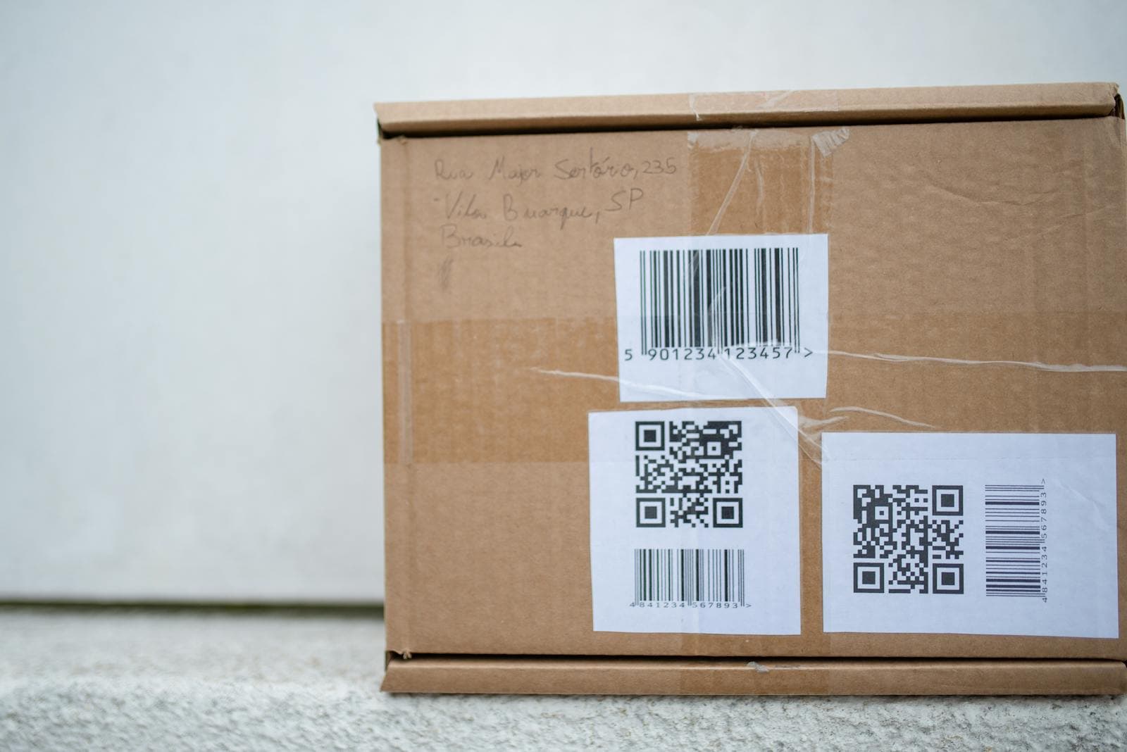 Cardboard delivery package with QR codes and a barcode shipping label.