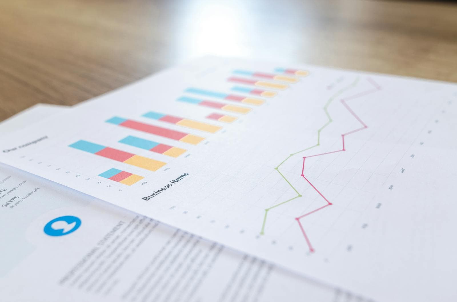 Printed business documents with line charts and bar graphs on a wooden desk.